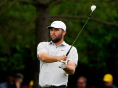 Scottie Scheffler Gives Sassy Response To LIV Golf Question Male golfer in a white cap and polo swinging a golf club on a grassy course, focused on the shot.