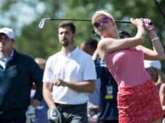 Paige Spiranac Approved To Wear Controversial Attire Woman in pink golf outfit mid-swing with a golf club, wearing visor and sunglasses, as spectators watch in the background.