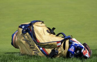 TaylorMade Qi4D Fairways: Tour vs Core — The Real Difference Tan leather golf bag with blue straps resting on a grassy golf course.