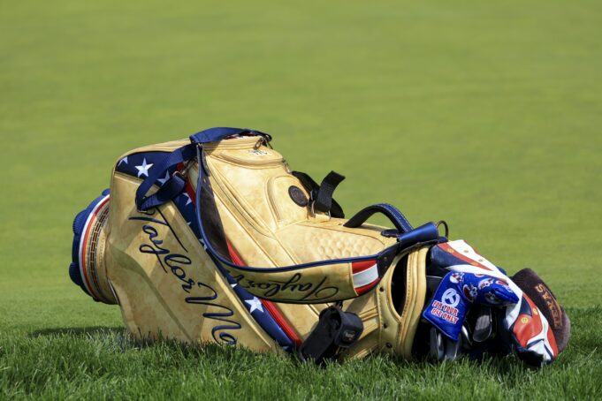 Tan leather golf bag with blue straps resting on a grassy golf course.
