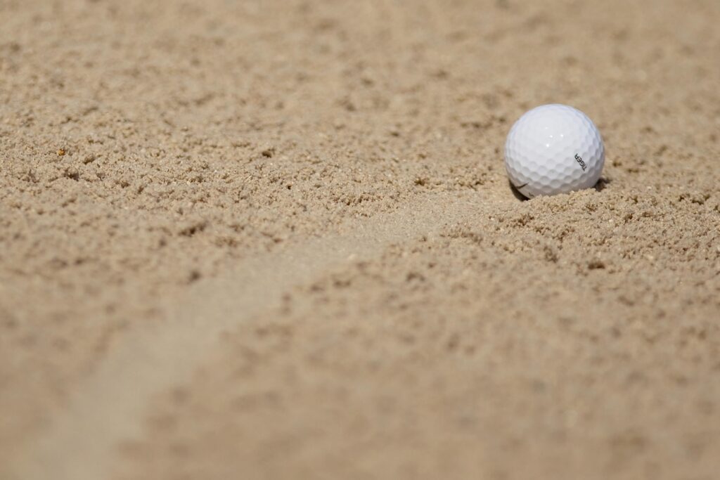 White golf ball partially buried in soft sand in a bunker, ready for a shot.