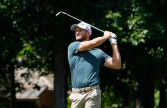 Wyndham Clark Blasts Crowd After Abuse at the US Open Male golfer in a teal shirt mid-swing with a golf club on a sunny course.