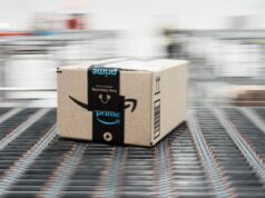 30+ Of The Best Amazon Prime Day Golf Deals I Have Spotted In 2026 Brown Amazon cardboard box on a moving conveyor belt in a warehouse, blurred background conveys motion