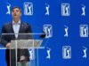 PGA Tour Unveils Two-Track System for 2028 Man in a dark suit giving a speech at a clear podium with a microphone against a blue PGA TOUR backdrop.