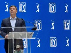 PGA Tour Unveils Two-Track System for 2028 Man in a dark suit giving a speech at a clear podium with a microphone against a blue PGA TOUR backdrop.