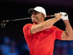Tiger Woods Introduces Major PGA Tour Reforms in Rare Appearance Male golfer in a red polo shirt and white cap mid-swing, gripping a golf club against a dark background.