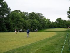 Indiana Rookie Emerges as LPGA’s Sole Left-Handed Player Golf course with several players walking and carrying golf bags near lush trees, a green fairway in the distance.