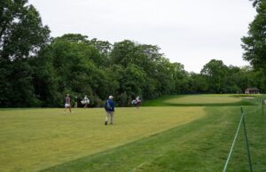 Indiana Rookie Emerges as LPGA’s Sole Left-Handed Player Golf course with several players walking and carrying golf bags near lush trees, a green fairway in the distance.