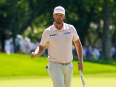 Clark Triumphs with Resilience at US Open Golfer walking on a sunny green course, wearing a pale pink polo and a white cap with a T-Mobile logo, holding a golf club.