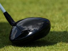 Just Announced: Tour Edge Exotics Reveals New Mini Driver Tech Close-up of a glossy black golf driver head on green grass with a light gray shaft visible nearby.