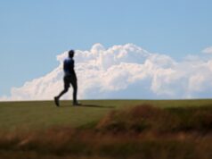 Shinnecock Hills Qualifiers Secure Spots at The Masters and US Open Blurry silhouette of a person walking on a grassy hill against a blue sky with fluffy clouds.