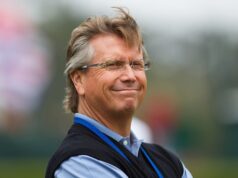 Scotty Cameron GOLO 6 Makes Traditional Putters Obsolete Smiling middle-aged man with gray hair and glasses outdoors, wearing a light blue shirt and dark vest with a blue lanyard.